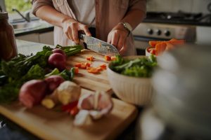 closeup of young female hands chopping fresh vegetables on chopping board while in modern kitchen preparing a healthy meal to boost immune system and fight off coronavirus